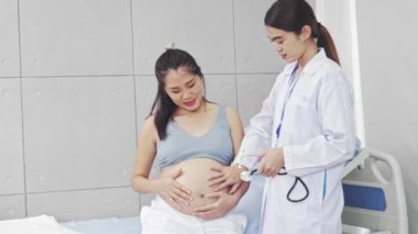 Doğum uzmanı, anne karnındaki fetüs sağlığını kontrol etmek için steteskop kullanıyor. Kalp atışlarını ölçüyor ve hastane muayene odasındaki fetal ve anne sağlığını değerlendiriyor..