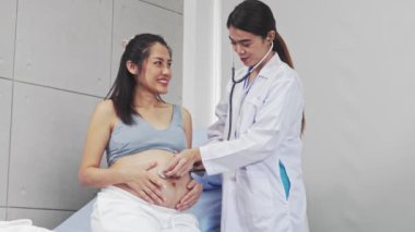 Doğum uzmanı, anne karnındaki fetüs sağlığını kontrol etmek için steteskop kullanıyor. Kalp atışlarını ölçüyor ve hastane muayene odasındaki fetal ve anne sağlığını değerlendiriyor..