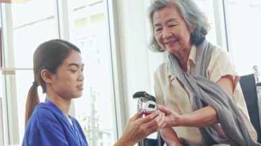 Hastane koğuşunda tekerlekli sandalyede yaşlı bir kadına bakan kadın hemşire, onları anlamasına yardımcı olması için oral kullanım ve son kullanma tarihi etiketleri için hapları tartışıyor..