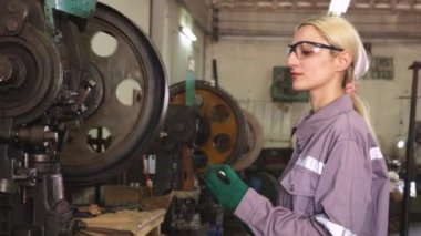 Güvenlik gözlüğü takan kadın torna operatörü metal ve güvenlik kulaklıkları gürültüsüne karşı koruyucu, parça üretim tesisinde ince metal levha damgalama makinelerini dikkatle kontrol ediyor..