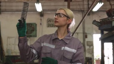 Güvenlik gözlüğü takan kadın torna operatörü, sanayi parçaları imalatında yedek parça olarak sertlik ve esnekliği kontrol etmek için bobin yayı tutuyor..