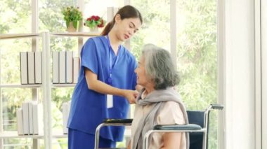 Hemşire, yaşlı hastayı iyi hissetmesi için eşarbını düzgünce düzelterek ve baş parmağını kaldırarak tekerlekli sandalyedeki yaşlı hastaya bakımı ve sağlığıyla ilgilenir..