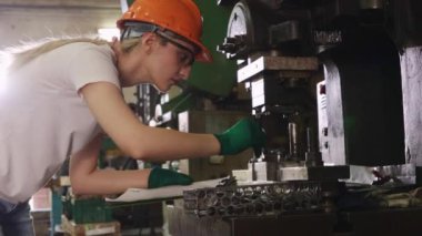 Sert şapka ve güvenlik gözlüğü takan kadın torna operatörü, verimli bir işletme sağlamak için yedek parça üretim tesisinde metal levha damgası için endüstriyel makineleri denetlemek için İngiliz anahtarı kullanıyor..