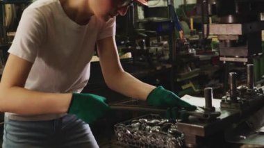 Sert şapka ve güvenlik gözlüğü takan kadın torna operatörü, verimli bir işletme sağlamak için yedek parça üretim tesisinde metal levha damgası için endüstriyel makineleri denetlemek için İngiliz anahtarı kullanıyor..