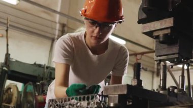 Sert şapka ve güvenlik gözlüğü takan kadın torna operatörü, verimli bir işletme sağlamak için yedek parça üretim tesisinde metal levha damgası için endüstriyel makineleri denetlemek için İngiliz anahtarı kullanıyor..