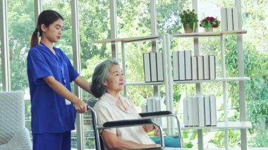 Kadın hemşire, iyileşme odasında tekerlekli sandalyedeki yaşlı hasta bir kadına bakıyor. Hemşire yaşlı ve hasta kadının endişelerini dindirmesine ve akıl sağlığını düzeltmesine yardım ediyor..