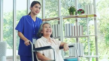 Kadın hemşire, iyileşme odasında tekerlekli sandalyedeki yaşlı hasta bir kadına bakıyor. Hemşire yaşlı ve hasta kadının endişelerini dindirmesine ve akıl sağlığını düzeltmesine yardım ediyor..