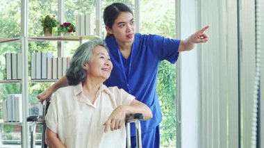 Kadın hemşire, iyileşme odasında tekerlekli sandalyedeki yaşlı hasta bir kadına bakıyor. Hemşire yaşlı ve hasta kadının endişelerini dindirmesine ve akıl sağlığını düzeltmesine yardım ediyor..