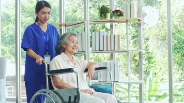 Hemşire, tekerlekli sandalyedeki yaşlı bir hastayı titizlikle giydirir ve onunla ilgilenir ve hasta eşarbının kendisini daha iyi hissetmesini sağlar..