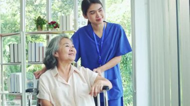 Hemşire, tekerlekli sandalyedeki yaşlı bir hastayı titizlikle giydirir ve onunla ilgilenir ve hasta eşarbının kendisini daha iyi hissetmesini sağlar..