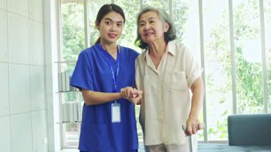 Kemik iltihabı olan yaşlı bir kadına bakan kadın hemşire, ayağa kalkmasına ve dikkatli yürümesine yardımcı olmak için bastona ihtiyaç duyar..