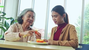 Yaşlı bir anne ile yetişkin kızının sağlıklı meyve yediği bir an. Yaşlı anne, kızının mutlu bir şekilde yemesi için hurma soymak için bıçak kullanır..