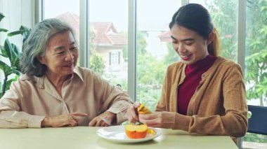 Yaşlı anne ve yetişkin kızı arasındaki sevgi, annesine sağlıklı meyveler veriyor. Kız, yaşlı annesinin mutlu bir şekilde yiyebilmesi için bıçak kullanıyor..