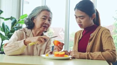Yaşlı bir anne ile yetişkin kızının sağlıklı meyve yediği bir an. Yaşlı anne, kızının mutlu bir şekilde yemesi için hurma soymak için bıçak kullanır..