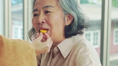 Kızı tarafından kendisine hurma yiyen yaşlı bir annenin mutlu yüzü: Yaşlı bir anne ile annesine değer veren ve ona minnettar olan yetişkin kızı arasındaki sevgi dolu an.