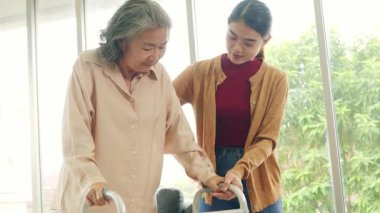 Kemik iltihabı olan yaşlı bir kadına bakan kadın hemşire, ayağa kalkmasına ve dikkatli yürümesine yardımcı olmak için bastona ihtiyaç duyar..