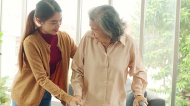 Kemik iltihabı olan yaşlı bir kadına bakan kadın hemşire, ayağa kalkmasına ve dikkatli yürümesine yardımcı olmak için bastona ihtiyaç duyar..