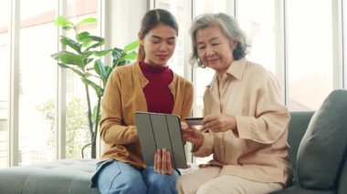 Kızı Asyalı yaşlı bir anneye tablet uygulamasından alışveriş yapmayı öğretiyor, ürünleri seçiyor ve kredi kartıyla kolayca ödüyor, her ikisi de alışverişi seviyor..