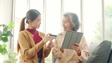 Kızı Asyalı yaşlı bir anneye tablet uygulamasından alışveriş yapmayı öğretiyor, ürünleri seçiyor ve kredi kartıyla kolayca ödüyor, her ikisi de alışverişi seviyor..