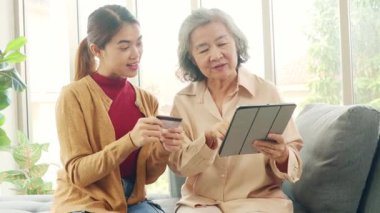 Kızı Asyalı yaşlı bir anneye tablet uygulamasından alışveriş yapmayı öğretiyor, ürünleri seçiyor ve kredi kartıyla kolayca ödüyor, her ikisi de alışverişi seviyor..