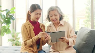 Kızı Asyalı yaşlı bir anneye tablet uygulamasından alışveriş yapmayı öğretiyor, ürünleri seçiyor ve kredi kartıyla kolayca ödüyor, her ikisi de alışverişi seviyor..