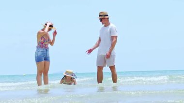 Mutlu aile yaz tatili: Baba kızını yukarıda tutuyor ve birlikte denizde oynamaktan hoşlanıyor, bu arada anne de onu kenardan neşelendiriyor..