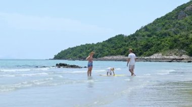 Mutlu aile yaz tatili: baba, anne ve kız denizde yürüyor, güneşli bir yaz gününde kumlu kumsalda seyahat ediyor..