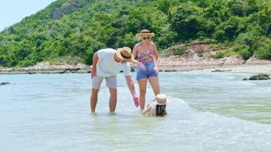 Mutlu aile yaz tatili: baba, anne ve kız denizde yürüyor, güneşli bir yaz gününde kumlu kumsalda seyahat ediyor..