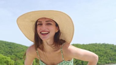 Güneş şapkalı güzel, uzun saçlı, mutlu, şık kısa elbiseler giyen, yeşil askısız, sevimli plaj kıyafeti giyen, yaz tatilinde dalgalara çarpan güzel bir kadın.