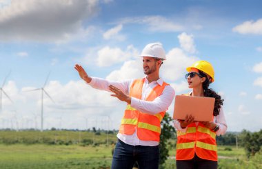 Erkek teknisyen kadın mühendisin rüzgar çiftliği projesindeki konuşmalarını uzaktan dinlediğini ve elinde dizüstü bilgisayarla uzun rüzgar türbini kulesini incelemeye hazırlandığını açıkladı..