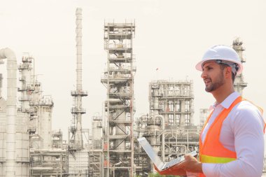 Sert şapka takan erkek mühendis iş platformunu kontrol etmek için dizüstü bilgisayar kullanarak petrol ve doğalgaz boru hattının güvenlik denetimini yapıyor ve önleyici bakım raporu kaydediyor..