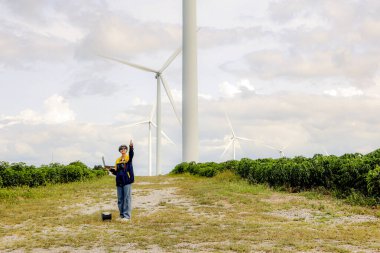 Rüzgâr türbini direğini işaret eden dizüstü bilgisayarı tutan kadın mühendis rüzgar türbini kurulum alanında elektrik üreten ve önleyici bakım yapan rotasyon bütünlüğünü kontrol ediyor..