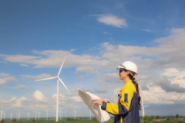 Rüzgâr çiftliğinde rüzgar enerjisi projesi planlayan kadın mimar elinde planlar ile çevre dostu konut binalarında kullanmak üzere elektrik dağıtım istasyonu tasarlıyor..