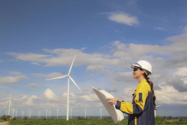 Rüzgâr çiftliğinde rüzgar enerjisi projesi planlayan kadın mimar elinde planlar ile çevre dostu konut binalarında kullanmak üzere elektrik dağıtım istasyonu tasarlıyor..