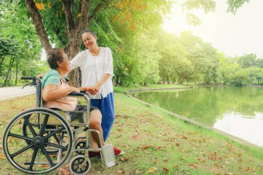 Bacakları kesilmiş ve tekerlekli sandalyede tedavi gören yaşlı bir kadını tedavi eden kız ya da hemşire sakatlığını gidermek için protez bacağını tutuyor..