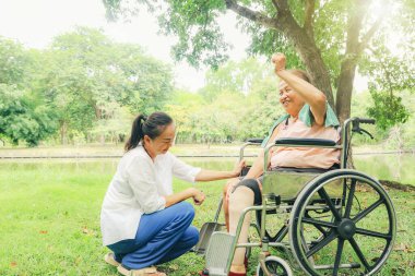 Bacakları kesilmiş ve tekerlekli sandalyede tedavi gören yaşlı bir kadını tedavi eden kız ya da hemşire sakatlığını gidermek için protez bacağını tutuyor..