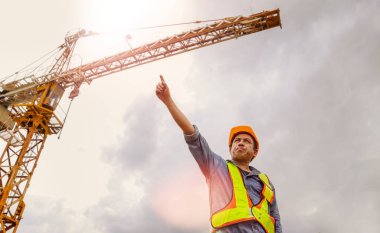 İnşaat alanındaki yüksek binadaki vinç operatörü erkek sürücü kolları çapraz ve güvenli bir şekilde duruyor: İşçiler yüksek bina inşaatında çalışıyorlar.