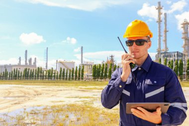Erkek mühendis merdivenlerden çıkar ve yukarıdan güvenlik teftiş alanına bakar. Petrol ve gaz boru hattı koruyucu bakım için telsiz raporu tutar..