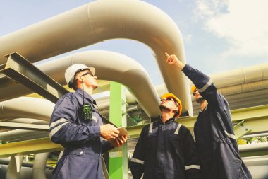 Erkek mühendisler ve teknisyenler, güvenlik önleyici bakım tesisatını denetlemek için bölgeye giriyor. Petrol ve gaz boru hatları, güvenlik için boru kaynaklarını denetleyen teknisyenlere işaret ediyor..