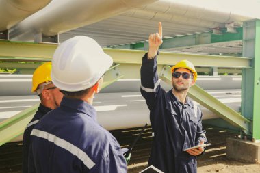 Erkek mühendisler ve teknisyenler, güvenlik önleyici bakım tesisatını denetlemek için bölgeye giriyor. Petrol ve gaz boru hatları, güvenlik için boru kaynaklarını denetleyen teknisyenlere işaret ediyor..