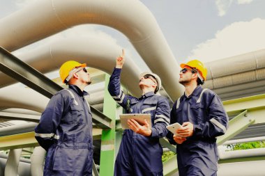 Erkek mühendisler ve teknisyenler, güvenlik önleyici bakım tesisatını denetlemek için bölgeye giriyor. Petrol ve gaz boru hatları, güvenlik için boru kaynaklarını denetleyen teknisyenlere işaret ediyor..