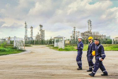 Erkek mühendisler ve teknisyenler, dış tesislerdeki basınçlı petrol ve doğalgaz boru hattının güvenlik teftiş alanına giriyor ve önleyici bakım çalışmalarını tartışıyorlar..