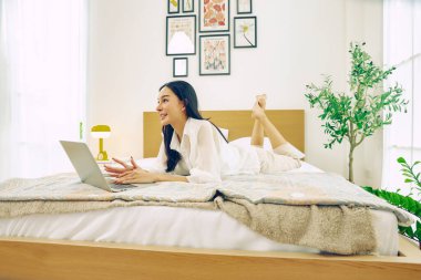 Özgür bir hayat yaşayan Asyalı güzel bir kadın. Yatakta uzanıyor, dizüstü bilgisayarla oynuyor, internetten alışveriş yapıyor, sohbet ediyor, sipariş veriyor, dizüstü bilgisayardaki ürünlere bakıyor, mutlu bir şekilde gülümsüyor..