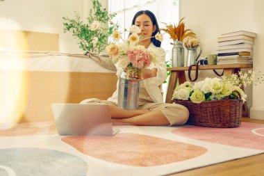 Asyalı bir kadın tatilini evinde, yatak odasında geçiriyor. Evini güzelce süslemek için vazoda pastel renkli plastik güller düzenliyor..