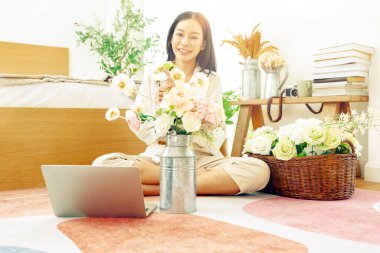 Asyalı bir kadın tatilini evinde, yatak odasında geçiriyor. Evini güzelce süslemek için vazoda pastel renkli plastik güller düzenliyor..