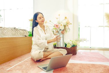 Asyalı bir kadın tatilini evinde, yatak odasında geçiriyor. Evini güzelce süslemek için vazoda pastel renkli plastik güller düzenliyor..