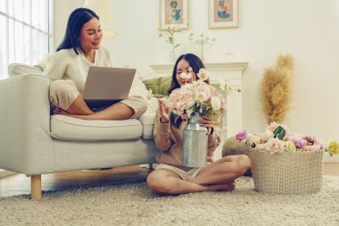 Boş zaman yaşam tarzı aktiviteleri evde suni çiçekler düzenlemeler güzel pastel renkler suni çiçekler ve kanepede oturmuş dizüstü bilgisayarla oynayan bir bayan arkadaş keyfine bakıyor..