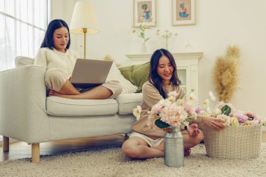 Boş zaman yaşam tarzı aktiviteleri evde suni çiçekler düzenlemeler güzel pastel renkler suni çiçekler ve kanepede oturmuş dizüstü bilgisayarla oynayan bir bayan arkadaş keyfine bakıyor..