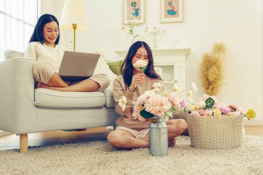 Boş zaman yaşam tarzı aktiviteleri evde suni çiçekler düzenlemeler güzel pastel renkler suni çiçekler ve kanepede oturmuş dizüstü bilgisayarla oynayan bir bayan arkadaş keyfine bakıyor..