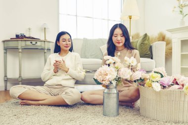 İki Asyalı kadın arasında evde suni çiçekleri düzenlemek için ücretsiz günlük yaşam aktivitesi. Renkli pastel çiçekler ve su içen bayan arkadaş..